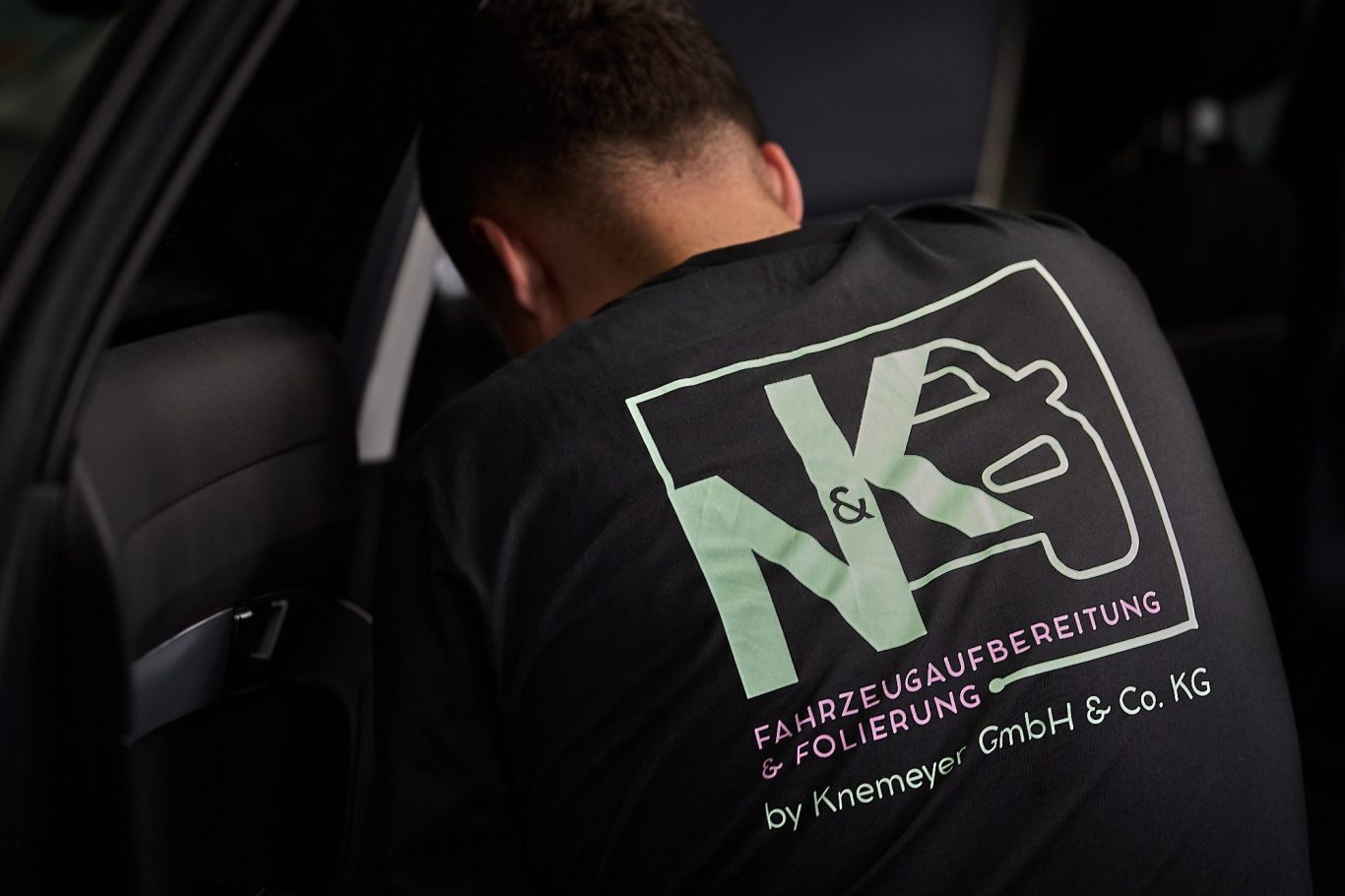 Person in einem schwarzen Shirt mit dem Aufdruck "NK - Kfz-Meisterbetrieb" bei der Arbeit.