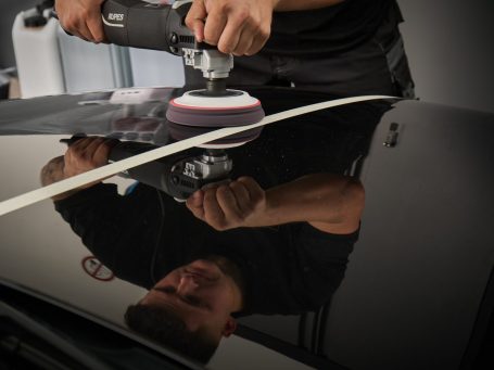 Person verwendet eine Poliermaschine auf einer glänzenden schwarzen Autolackoberfläche.