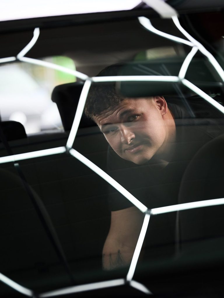 Mann sitzt im Auto, betrachtet reflektierende Hexagonalstruktur.